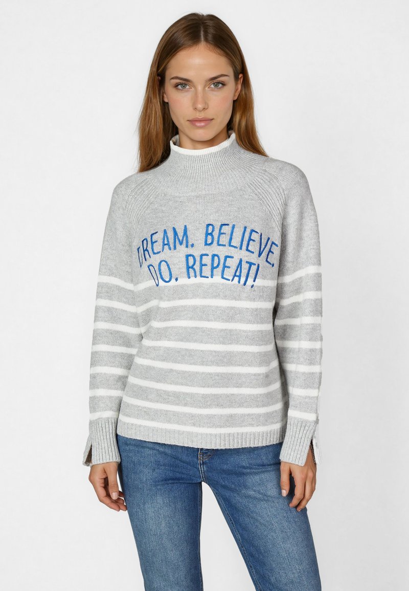 Gray sweater with white stripes, high neck, and ribbed cuffs. Embroidered text in blue reads, “DREAM. BELIEVE! DO. REPEAT!”
