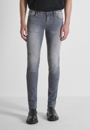 Jeans en denim gris ajustés, avec des zones décolorées, cinq poches, et une fermeture à bouton et zip, associés à des bottes noires.
