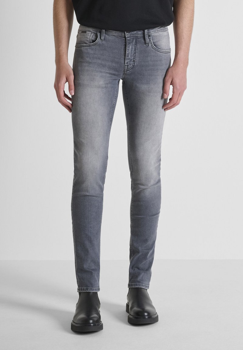 Jeans in denim grigio con vestibilità slim, caratterizzati da aree scolorite, cinque tasche e chiusura con bottone e zip, abbinati a stivali neri.