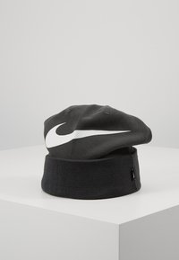 Cappello di maglia nera con orlo piegato, caratterizzato da un prominente logo Nike swoosh bianco sul davanti. Design semplice con texture liscia.