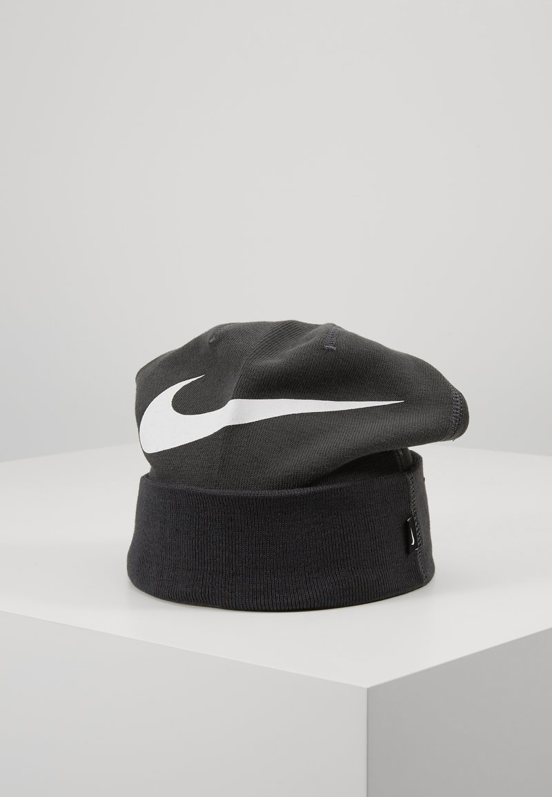 Cappello di maglia nera con orlo piegato, caratterizzato da un prominente logo Nike swoosh bianco sul davanti. Design semplice con texture liscia.