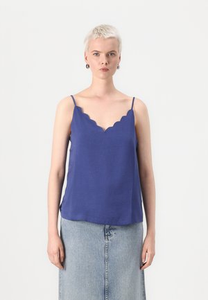 Top in raso viola con bordi scallop, realizzato in tessuto leggero, caratterizzato da spalline sottili e una vestibilità ampia, abbinato a una gonna di denim chiaro.