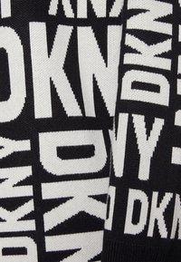 Stickad tröja med ett svartvitt mönster som har stor, djärv text. Materialet verkar mjukt och strukturerat med en kontrasterande färgsättning.