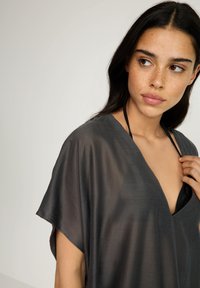 Sivi prozirni kaftan s V-izrezom i kratkim rukavima, lagani materijal i ležeran kroj, otkrivajući crni bikinij.