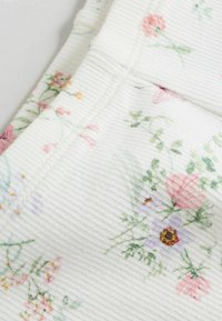 Tela acanalada con estampado floral en blanco con flores en tonos pastel. Presenta detalles en rosa, amarillo y verde, creando una superficie ligera y texturizada.