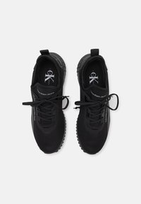 Černé sportovní boty s síťovaným svrškem, šněrovacím designem, polstrovaným límcem a gumovou podrážkou s malými kulatými akcenty. Logo vytištěné na bocích.