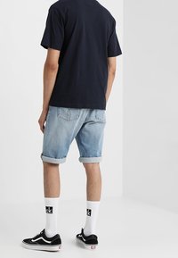 Marinblå t-shirt, ljusblå denimshorts med uppvikta ben, svarta sneakers och vita strumpor med logotyp, sedd bakifrån.