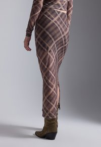 Lang, tettsittende kjole i brun med rutemønster, med lange ermer, en sidesplit, og brukt med olivengrønne hælboots.