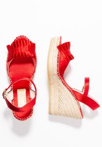 Sandalias de esparto rojas con parte superior de satén con volantes, tacón de yute y correa en el tobillo. Textura suave y diseño elegante.