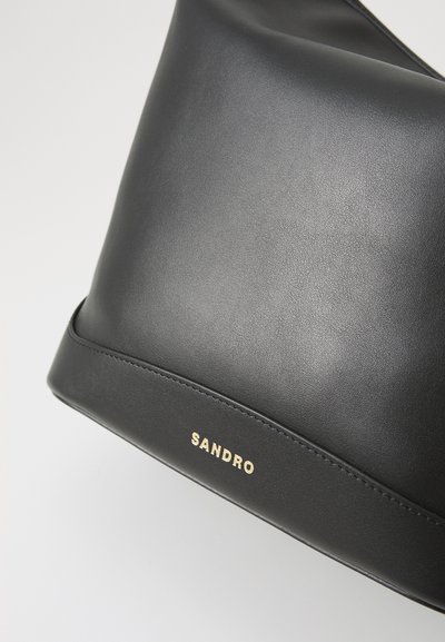 Must mustrassast mustrast, millel on siledat ja saatusmised pinnad; kuldne, reljeefne "SANDRO" logo ning minimalism.
