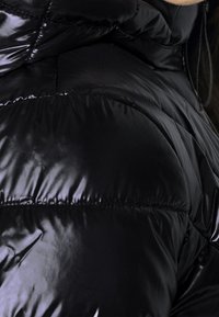 Czarna kurtka puchowa o błyszczącym wykończeniu, z pikowanymi sekcjami, wysokim kołnierzem oraz zamkami błyskawicznymi z przodu i w kieszeniach.