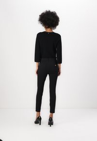 Black sweater with three-quarter sleeves, paired with black fitted pants. Notable details include a decorative back neckline and sleek heels.