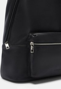 Zaino in pelle nera con una texture liscia, zip argentate e una tasca frontale con zip visibile. Design semplice e minimalista.