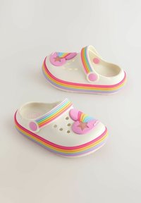 Valged klotsi-tossud vikerkaarevärvilise rihmaga, kaunistatud mänguliste südame ja tähega. Siledad pinnad koos õhutusavadega, mis tagavad hingavuse.