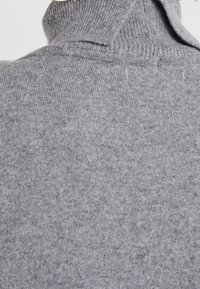 Pull à col roulé gris en tissu tricoté doux, avec un col haut et une finition texturée présentant des variations subtiles de couleur.