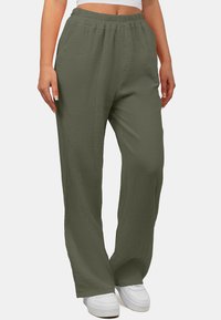 Lichte, loszittende, olijfgroene broek met een elastische tailleband, gestructureerde stof en een wijd beenontwerp. Draagt met witte sneakers.