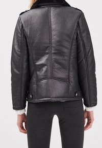 Černá kožená bunda s texturovaným povrchem, vybavená kožešinovým límcem, strukturovanými švy a cvočky na spodní straně.