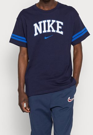Granatowy bawełniany t-shirt z napisem "NIKE" w odważnej białej czcionce, ozdobiony niebieskimi paskami na rękawach. Wygodne dopasowanie z okrągłym dekoltem.