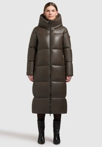 Lange, olijfgroene gewatteerde jas met een hoge kraag, geborduurd ontwerp, voorrits en lange mouwen, gecombineerd met zwarte laarzen tot de knie.