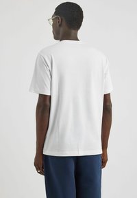 Biała bawełniana koszulka z krótkim rękawem, okrągłym dekoltem i gładką fakturą, w zestawie z ciemnoniebieskimi spodniami. Brak widocznych logo lub wzorów.