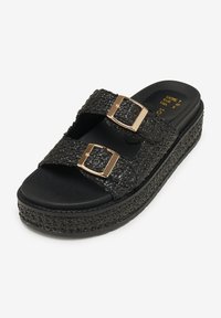 Infradito neri con platform, dotati di due cinturini intrecciati, fibbie dorate, materiale testurizzato e suola spessa nera.