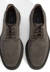 Une paire de chaussures en suede marron à lacets avec des bouts ronds et des semelles en caoutchouc foncé, vues de dessus sur un fond blanc.