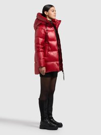 Czerwona pikowana kurtka puchowa z kapturem, z połyskującym wykończeniem. Modelka nosi czarną dzianinową spódnicę i czarne kozaki za kolano.