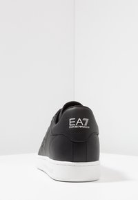 Svarta lädersneakers med vit sula, som visar bakvy och "EA7 Emporio Armani"-logotyp på hälen.