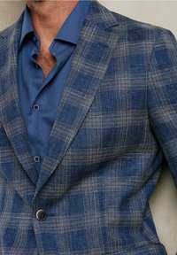 Blå rutig kavaj med en texturerad tyg, som har en ljusblå skjorta under, vilket visar en skräddarsydd passform och strukturerade slag.