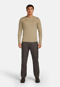 Camicia khaki a maniche lunghe con scollatura rotonda, abbinata a pantaloni cargo grigio scuro con tasche laterali e vestibilità ampia. Scarpe nere.