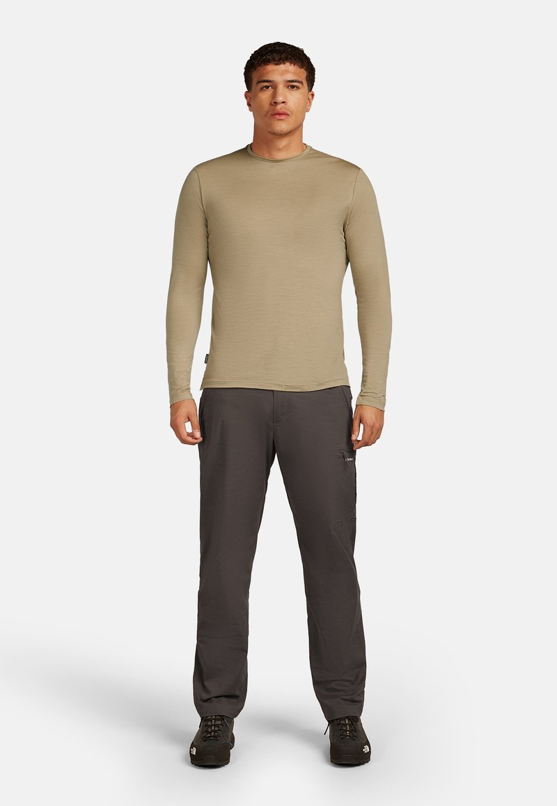 Camicia khaki a maniche lunghe con scollatura rotonda, abbinata a pantaloni cargo grigio scuro con tasche laterali e vestibilità ampia. Scarpe nere.