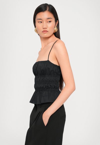 Black peplum top with adjustable spaghetti straps, featuring gathered texture and a fitted bodice, worn with high-waisted black pants.