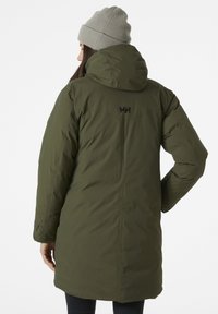Parka verde isolata con cappuccio removibile, dotata di un logo sulla parte posteriore e di una superficie liscia e texture. Berretto in grigio chiaro.