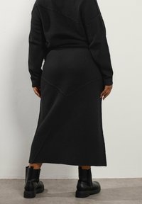 Mustakudottu kaksiosainen asu, jossa on ribbikuvio. Midi-hameessa on istuva vyötärö ja levenevä helma. Yhdistetty mustiin nilkkureihin.