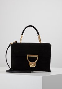 Mustan mokkanahkainen käsilaukku, jossa on rakenteellinen muotoilu, kultaiset yksityiskohdat, ylähihna ja irrotettava olkahihna. Siinä on etutasku sekä logo-yksityiskohta.