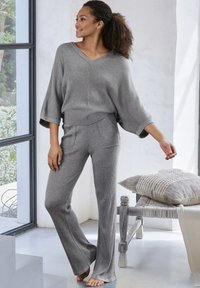 Grijze geribbelde knit loungewear set met een oversized top met V-hals en aansluitende broek. Zachte textuur met gespleten mouwen en brede broekspijpen.