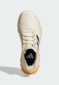 Chaussure de sport beige clair avec des rayures noires, tige texturée et semelle en caoutchouc orange. Elle dispose d'une languette rembourrée et d'un détail de logo sur la semelle intérieure.
