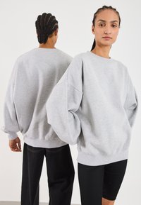 Felpa oversized grigia chiara con spalle scese e polsini a coste, abbinata a pantaloni neri. Tessuto morbido, vestibilità rilassata.