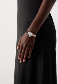 Montre-bracelet en argent et ton or avec un cadran rond, un cadran blanc et un mélange d'accents métalliques et noirs sur le bracelet. Présente un design texturé.