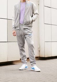 Grå Nike-träningsdress med vita ärmar, innehållande en ljuslila t-shirt. Blå logotypdetaljer och sneakers med blå swoosh.