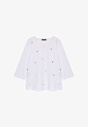 Camisa blanca de manga larga con cuello redondo, adornada con detalles dispersos en dorado, rojo y negro, y un corte holgado. Material de algodón suave.