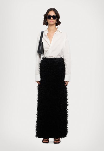 Jupe maxi en plumes noires avec un design texturé et superposé ; assortie à une chemise blanche à boutons et des lunettes de soleil noires. Complétée par un sac noir.