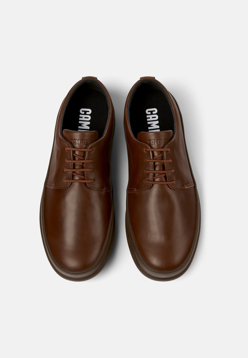 Bruna läderskor med en slät yta, rund tå, fem hål snörningsdesign och en svart vadderad innersula med "CAMPER"-märkning.