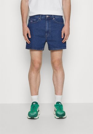 Shorts di jeans blu scuro con cinque tasche, chiusura con bottone metallico e orlo sfrangiato. Indossati con sneakers bianche e verdi.