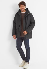 Dark gray puffer jacket with a hood, front snap button closure, and side pockets, paired with a brown sweater and dark jeans. Casual footwear.