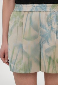 Shorts met een elastische tailleband, gemaakt van lichtgewicht stof in beige, met een palmbladpatroon in tinten groen en blauw.