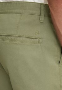 Olive green trousers, made of soft fabric, featuring a back pocket with subtle stitching and a small embroidered logo on the waistband.