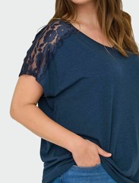 Navy blue short-sleeve top with lace floral accents on shoulders. Soft fabric with relaxed fit and side pocket detail.