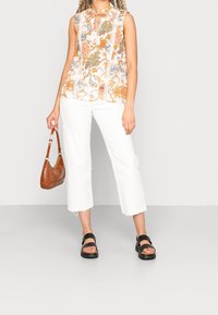 Haut sans manches à motif floral avec une encolure à découpe en forme de goutte et un jean blanc. Les accessoires comprennent un sac à main marron embossé crocodile et des sandales compensées noires.