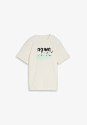 T-shirt à manches courtes de couleur crème avec un texte noir et bleu clair indiquant « DOING » en police grasse et abstraite sur le devant.